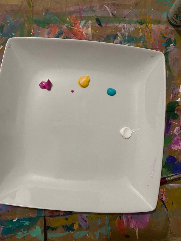 a white plate with paint in yellow, magenta and teal